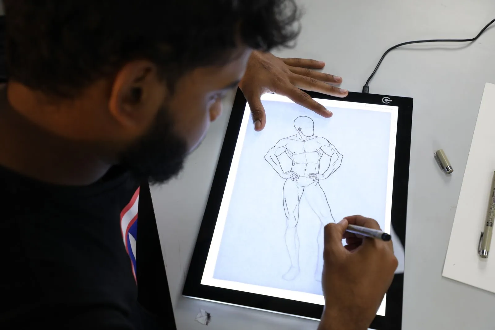 Illustrator sketching a superhero figure on a digital lightboard in an art studio setting.